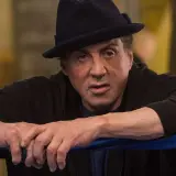 Sylvester Stallone jako Rocky Balboa, w czarnym kapeluszu i bluzie, opiera się o linę ringu.