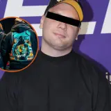 Mężczyzna w czarnej bluzie z kapturem i czapką. W okręgu na jego bluzie widnieje grafika z postacią przypominającą umpa lumpa, trzymającą stos pieniędzy.