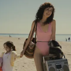 Rose Byrne w różowym kostiumie kąpielowym na plaży z córką, niosąc torbę i boombox.