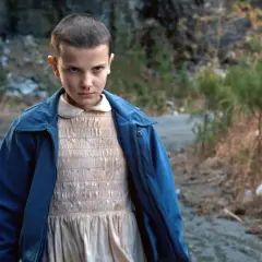 Nastka z Stranger Things, z nosem krwawiącym, stoi na tle kamienistego krajobrazu.