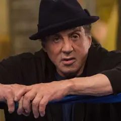 Sylvester Stallone jako Rocky Balboa, w czarnym kapeluszu i bluzie, opiera się o linę ringu.