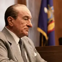 Robert De Niro w garniturze, w sali sądowej, przypomina jego role w wielu filmach.