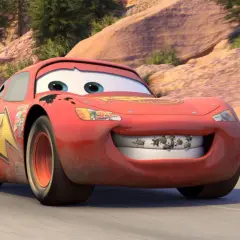 Błyskawica McQueen z "Auta 4" na drodze. Jego uśmiech zdobią owady, a na karoserii widać ślady przygód.