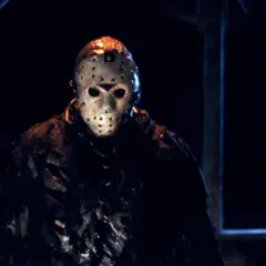 Jason Voorhees w swojej charakterystycznej masce hokejowej, stojący w mroku.