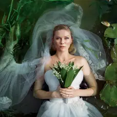 Kirsten Dunst w sukni ślubnej leży w wodzie wśród lilii wodnych i traw. Scena przypomina kadr z jej filmów.
