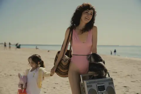 Rose Byrne w różowym kostiumie kąpielowym na plaży z córką, niosąc torbę i boombox.