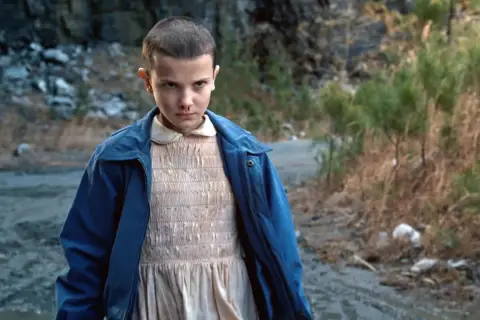Nastka z Stranger Things, z nosem krwawiącym, stoi na tle kamienistego krajobrazu.