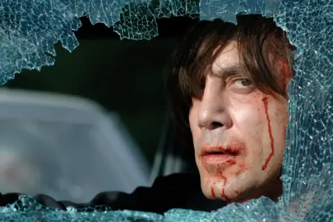 Javier Bardem w filmach, z zakrwawioną twarzą, patrzy przez pękniętą szybę.