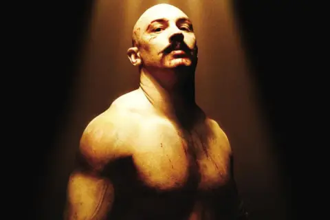 Tom Hardy jako Bronson, w stylu filmów Charlesa Bronsona. Zgolona głowa, wąsy i blizny.