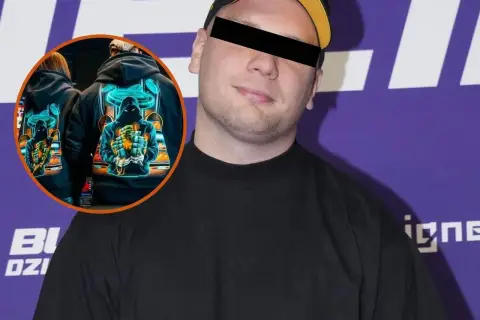 Mężczyzna w czarnej bluzie z kapturem i czapką. W okręgu na jego bluzie widnieje grafika z postacią przypominającą umpa lumpa, trzymającą stos pieniędzy.