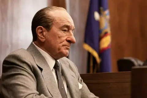 Robert De Niro w garniturze, w sali sądowej, przypomina jego role w wielu filmach.