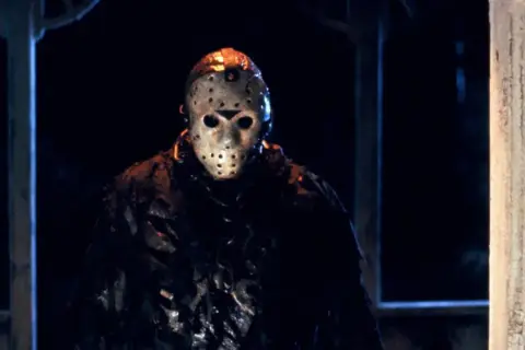 Jason Voorhees w swojej charakterystycznej masce hokejowej, stojący w mroku.