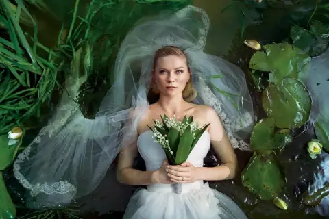Kirsten Dunst w sukni ślubnej leży w wodzie wśród lilii wodnych i traw. Scena przypomina kadr z jej filmów.