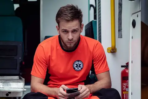 Młody ratownik medyczny Kuba, na sygnale, siedzi w karetce, trzymając telefon.