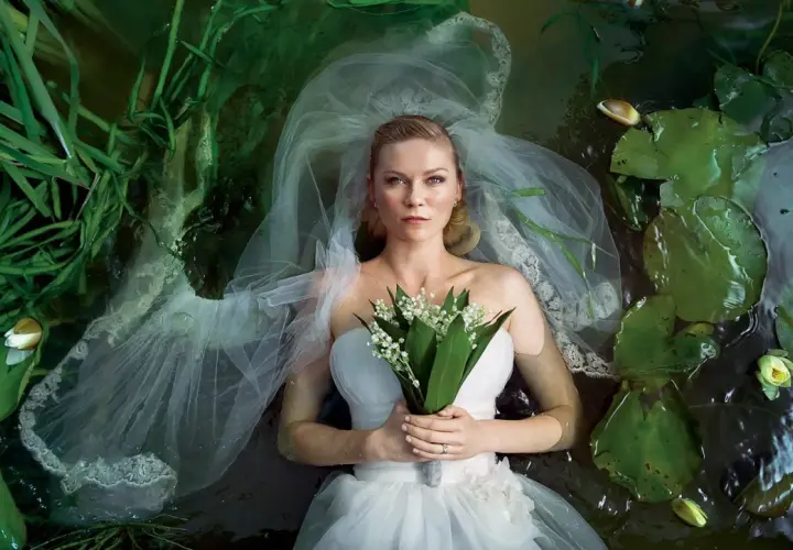 Kirsten Dunst w sukni ślubnej leży w wodzie wśród lilii wodnych i traw. Scena przypomina kadr z jej filmów.