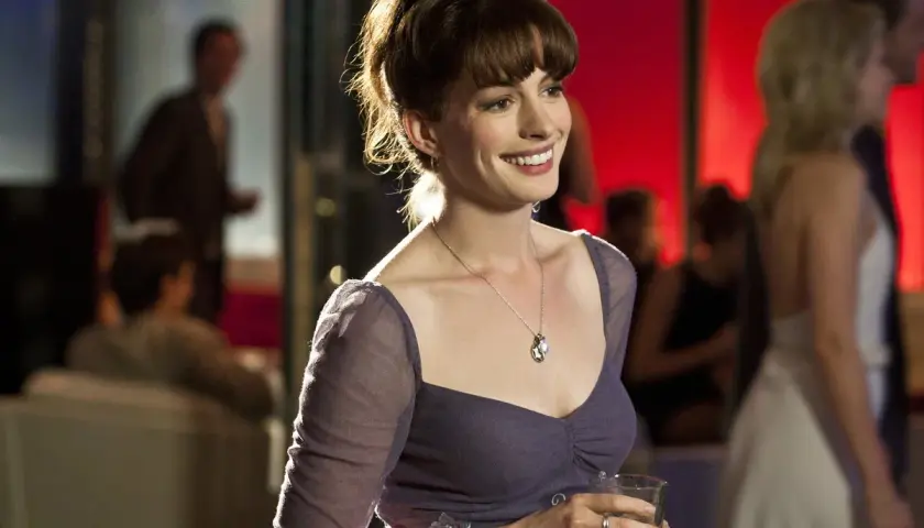 Anne Hathaway w filmie, uśmiechnięta, trzymająca drinka.
