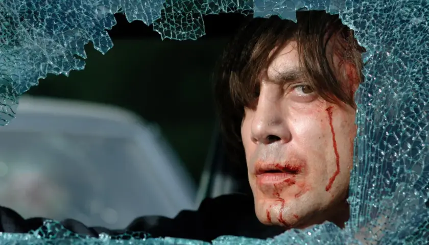 Javier Bardem w filmach, z zakrwawioną twarzą, patrzy przez pękniętą szybę.