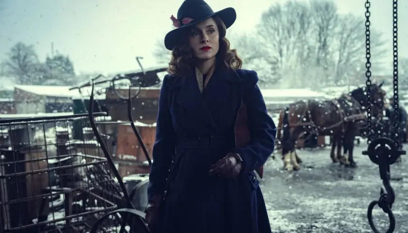 Elegancka kobieta w kapeluszu i płaszczu, w zimowej scenerii, jak z filmu Peaky Blinders.