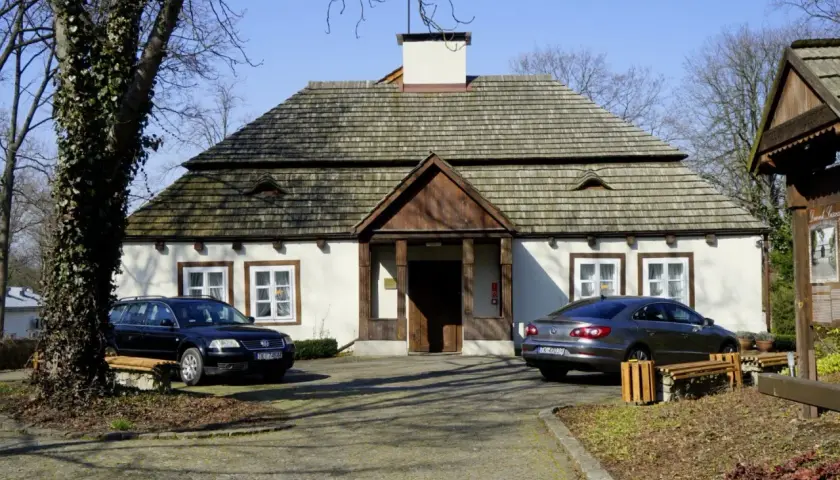 Dom z drewnianym dachem i dwoma samochodami przed wejściem.