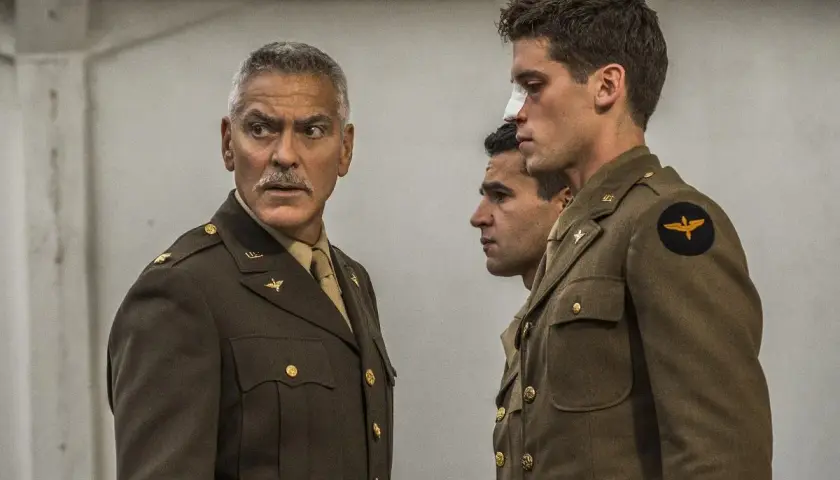 George Clooney w mundurze, obok dwóch młodych żołnierzy. Jeden z nich ma opatrunek na nosie. Scena jak z paragrafu 22.