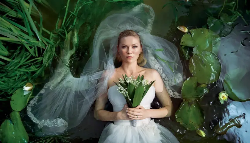 Kirsten Dunst w sukni ślubnej leży w wodzie wśród lilii wodnych i traw. Scena przypomina kadr z jej filmów.