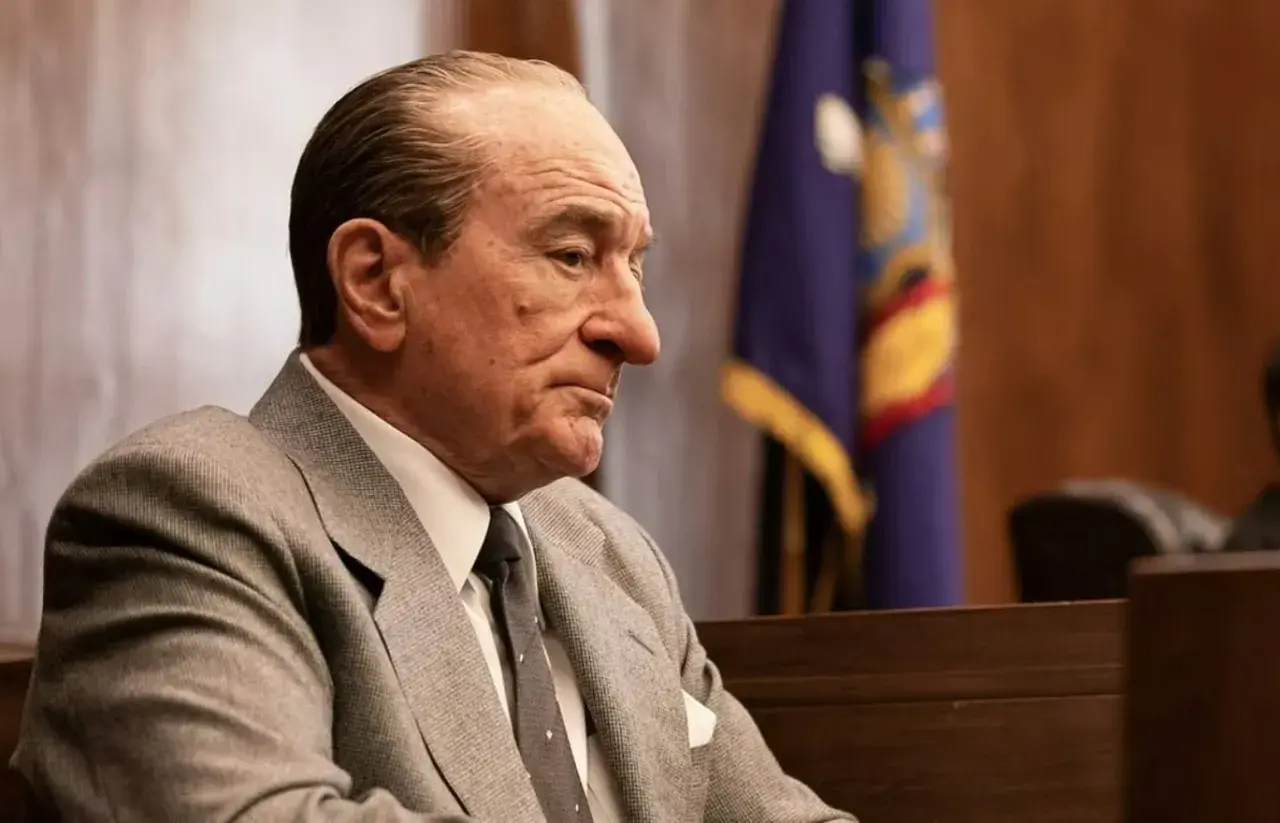 Robert De Niro w garniturze, w sali sądowej, przypomina jego role w wielu filmach.