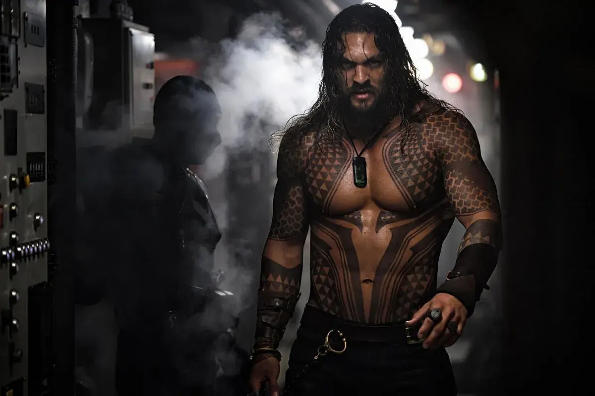 Aquaman z tatuażami na torsie i ramionach, w otoczeniu dymu.