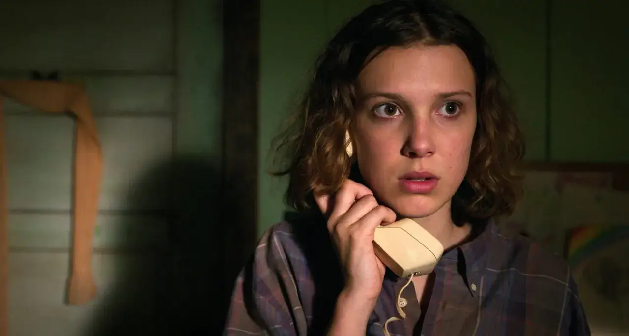 Nastka z Stranger Things trzyma słuchawkę telefonu, jej oczy są szeroko otwarte, jakby usłyszała coś niepokojącego.