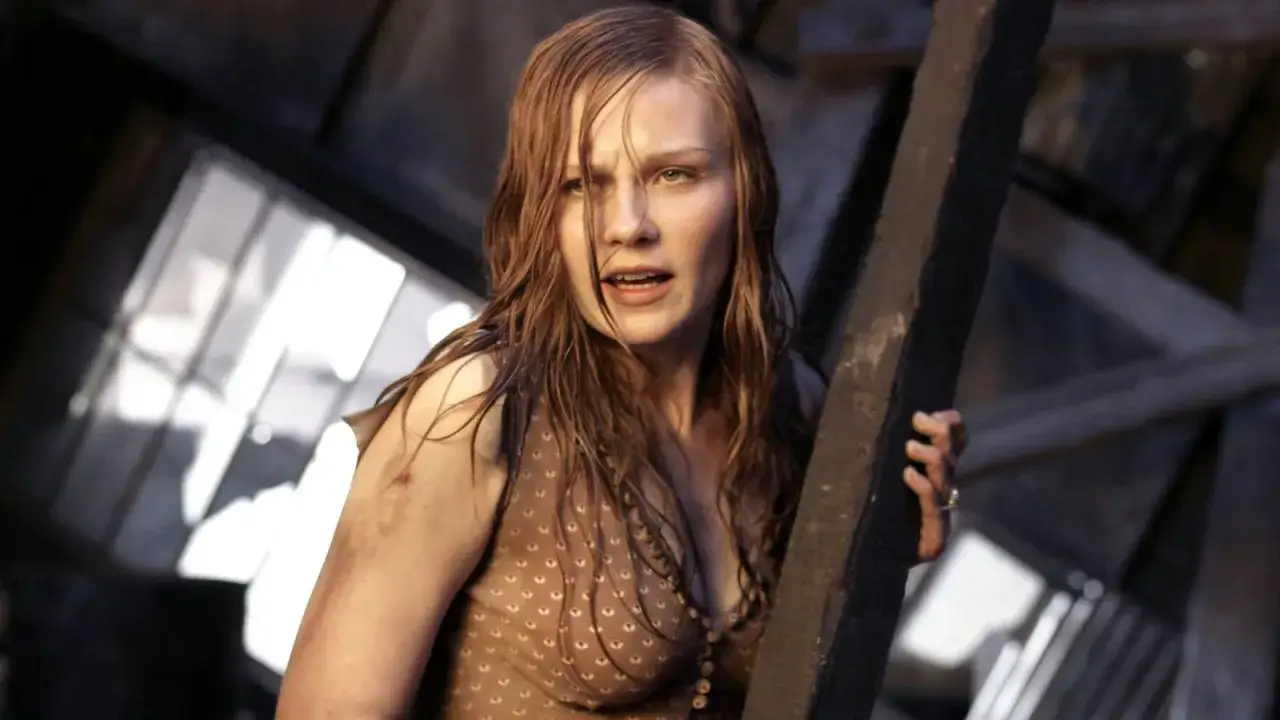 Kirsten Dunst w filmach, w dramatycznej scenie, z mokrymi włosami i wyrazem strachu na twarzy, trzyma się drewnianej belki.