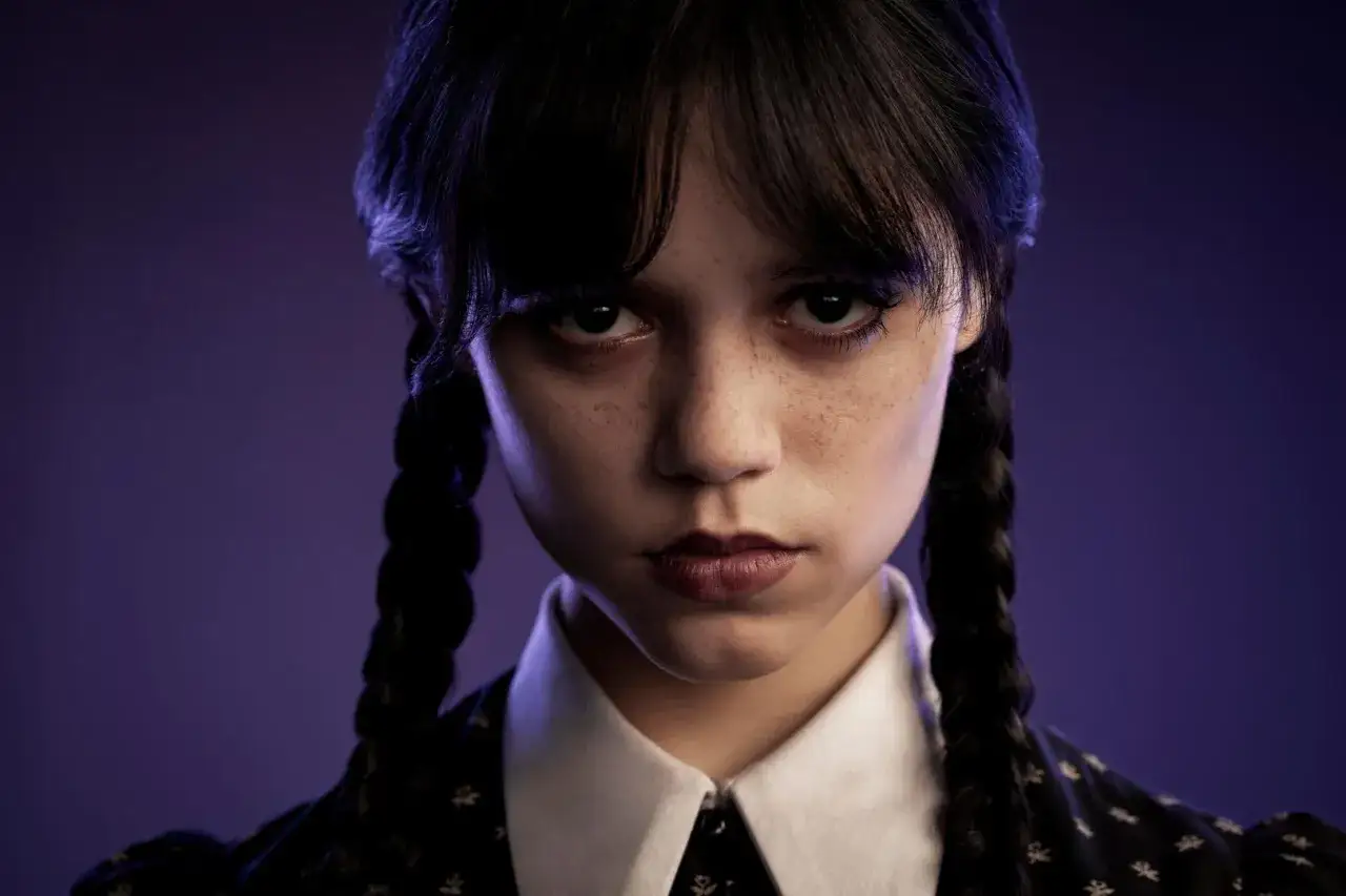 Jenna Ortega jako Wednesday Addams, aktorka z charakterystycznym spojrzeniem i warkoczami, na tle fioletowego światła.