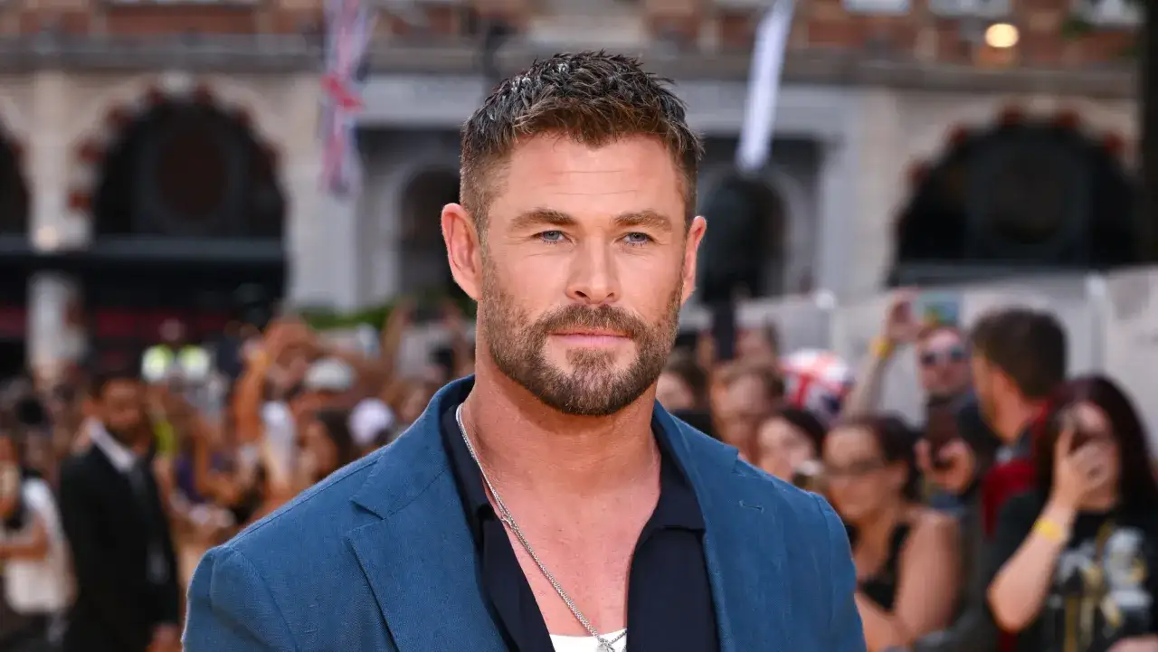 Chris Hemsworth, gwiazda wielu filmów, na premierze w niebieskiej marynarce. Tłum fanów w tle.