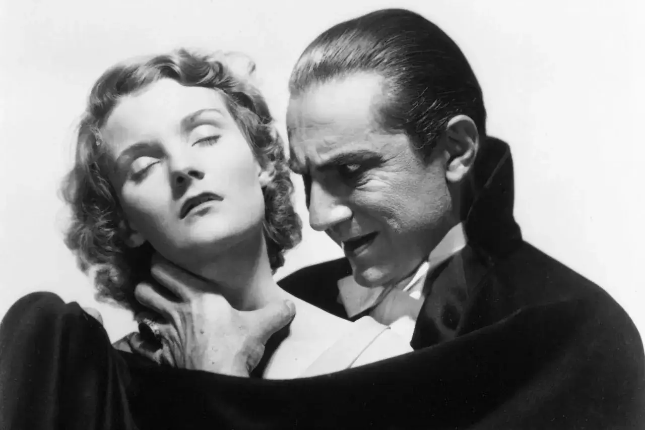 Dracula pochyla się nad kobietą, jego dłoń zaciska się na jej szyi. Jej oczy są zamknięte, jakby w transie.